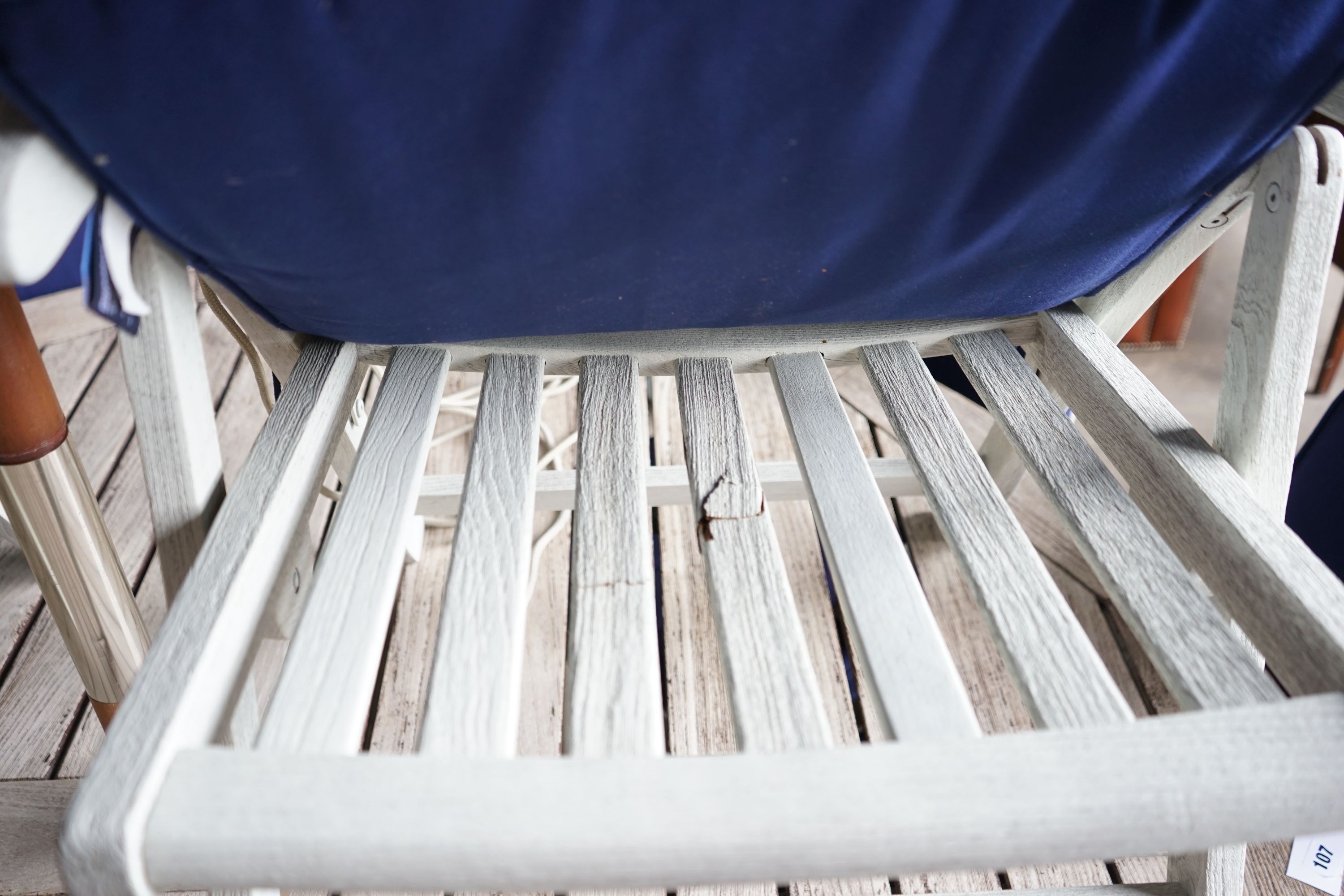 A large circular weathered teak garden table, diameter 180cm, height 72cm, eight painted teak folding chairs with seat pads and a blue canvas crank parasol